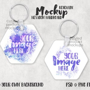 Puede incluir: Dos llaveros hexagonales blancos con anillas de metal plateadas. Los llaveros tienen un diseño de acuarela con detalles en morado y azul. El texto "YOUR IMAGE HERE" está impreso en ambos llaveros.