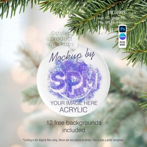 May include: A clear acrylic Christmas ornament mockup with a purple and blue design. The ornament is hanging in front of a blurred background with evergreen branches. The text "Mockup by SPM" and "Your Image Here" are visible.