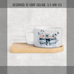 May include: White ceramic mug with a floral design featuring blue and peach flowers, a blue gift box, and a dark blue bow. The mug sits on a light brown wooden coaster. The mug is designed to crop square, 5:4 and 4:5.