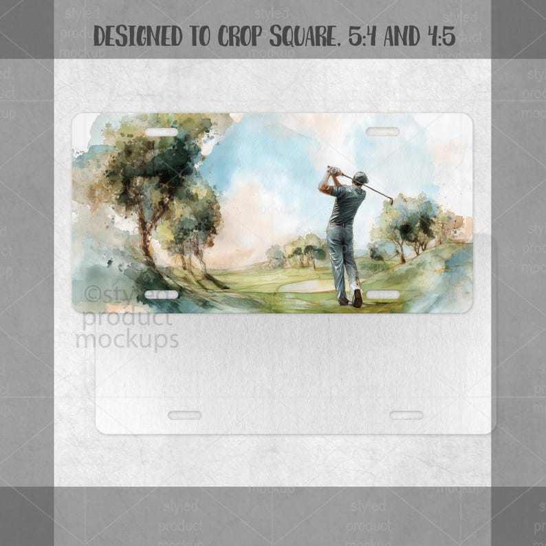 May include: A white license plate with a watercolour painting of a golfer swinging a club on a green golf course. The artwork includes trees, a blue sky, and a light green fairway. The plate has pre-drilled holes for mounting.