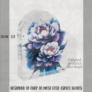 Pu&ograve; includere: Un blocco acrilico trasparente a forma di cuore con un motivo floreale ad acquerello. Presenta peonie bianche e viola e foglie blu. Il testo recita "DESIGNED TO CROP TO MOST ETSY ASPECT RATIOS".