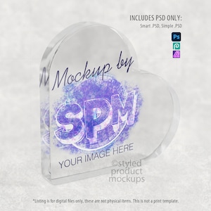 Pu&ograve; includere: Un blocco acrilico trasparente a forma di cuore con il testo "Mockup by SPM" e "YOUR IMAGE HERE" in viola e bianco. L'immagine include anche il testo "INCLUDES PSD ONLY: Smart .PSD, Simple .PSD".