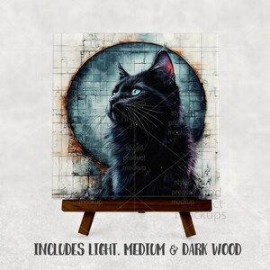 以下が含まれることがあります： 青い目の黒猫が描かれた正方形のアートプリント。円形のデザインのテクスチャード加工された背景に配置されています。プリントは小さな木製イーゼルに表示されています。下部のテキストは次のとおりです：INCLUDES LIGHT, MEDIUM & DARK WOOD.