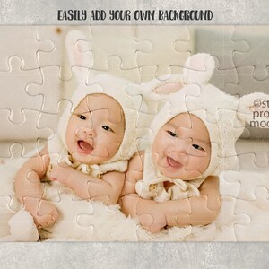 May include: Two babies wearing white bunny costumes with ears, lying on a white fuzzy blanket. The babies are looking at the camera and smiling. The image is a jigsaw puzzle with a white background.