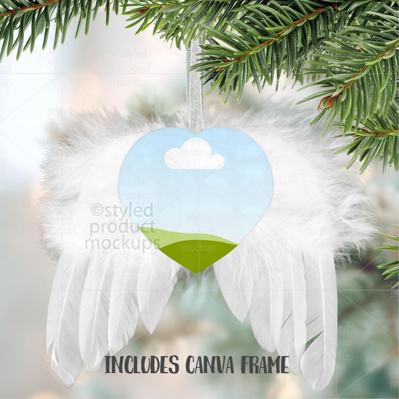 May include: Heart-shaped ornament with a sky and cloud design, surrounded by white feather wings. The ornament hangs from a silver ribbon, with the text "INCLUDES CANVA FRAME" at the bottom. The ornament is displayed against a backdrop of evergreen branches.