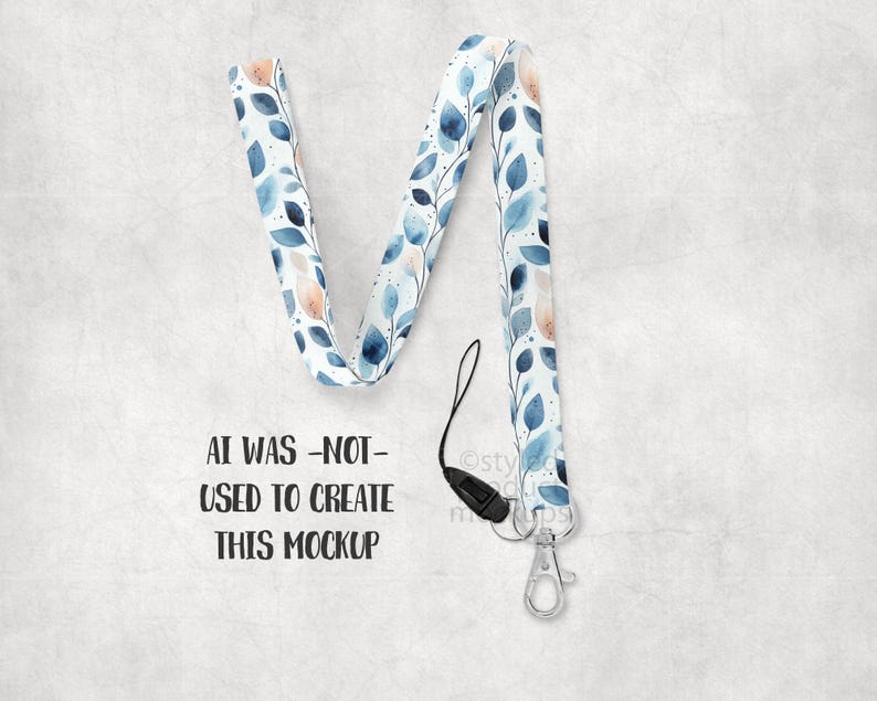 May include: A lanyard with a watercolor leaf pattern in shades of blue and peach. The lanyard has a black clasp and a silver-colored metal clip. The text "AI WAS -NOT- USED TO CREATE THIS MOCKUP" is printed on the background.