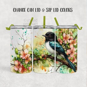 May include: Three white insulated tumblers with floral and bird designs. The center tumbler features a black and white bird perched on a branch with pink flowers. The text "CHANGE CAN LID & SIP LID COLORS" is at the top.