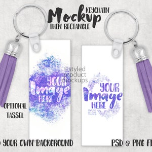 May include: Two thin rectangular keychains with silver rings and optional purple tassels. The left keychain features a purple and blue watercolor splash design with the text YOUR IMAGE HERE. The right keychain shows a purple floral wreath design with the text YOUR IMAGE HERE. Text includes Mockup Keychain Thin Rectangle, Optional Tassel, Add Your Own Background, and PSD & PNG Files.