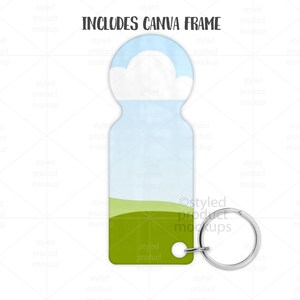 May include: A keychain with a sky and cloud design. The top portion features a blue sky with white clouds, transitioning to a light blue and green landscape. The text "INCLUDES CANVA FRAME" is at the top. A silver key ring is attached.