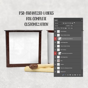 Op de afbeelding: Een digitaal product-mockup met een vierkante container met een donkerbruin frame en een wit middenpaneel, vergezeld van twee lichtgekleurde koekjesstokjes met chocoladedip. De tekst luidt PSD ORGANIZED LAYERS FOR COMPLETE CUSTOMIZATION.