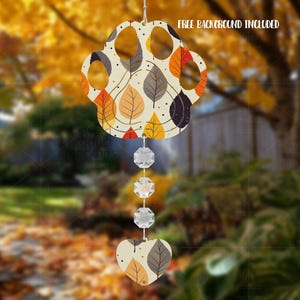 May include: A decorative wind chime with a paw-shaped top adorned with autumn leaf patterns in orange, yellow, and grey. It has three crystal beads and a heart-shaped base. The text "FREE BACKGROUND INCLUDED" is displayed.