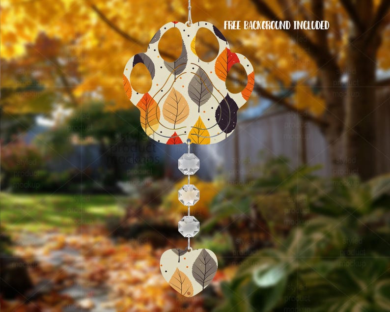 May include: A decorative wind chime with a paw-shaped top adorned with autumn leaf patterns in orange, yellow, and grey. It has three crystal beads and a heart-shaped base. The text "FREE BACKGROUND INCLUDED" is displayed.