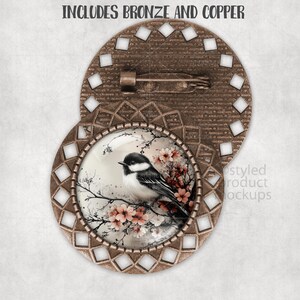 Op de afbeelding: Bronzen en koperkleurige broche met een vogel- en bloemmotief. De broche heeft een centraal beeld van een vogel op een tak met roze bloesems, omgeven door een decoratief frame. De tekst "INCLUDES BRONZE AND COPPER" staat bovenaan.