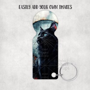 May include: Keyring featuring a black cat with blue eyes, set against a cityscape backdrop. The cat is the focal point, with detailed fur and a contemplative gaze. The keyring has a silver-colored ring and a white attachment. The text "EASILY ADD YOUR OWN IMAGES" is at the top.