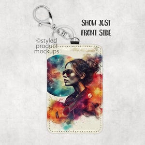 May include: A white leather keychain with a colorful abstract design featuring a woman with sunglasses and a guitar. The design includes a large circle with a galaxy-like pattern.