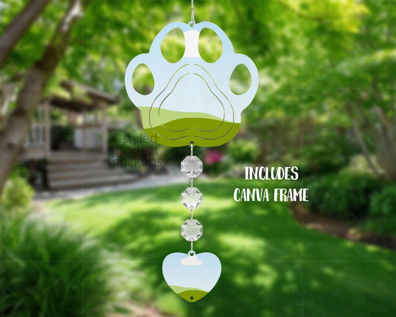 May include: A paw-shaped wind chime with a heart-shaped bottom, featuring a landscape design in shades of green and blue. The chime includes three crystal-like beads and the text "INCLUDES CANVA FRAME".