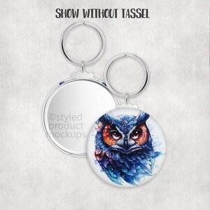 May include: Round keychain featuring a watercolor owl design in shades of blue, orange, and purple. The keychain has a silver metal ring and a blank, mirrored back. Text at the top reads "SHOW WITHOUT TASSEL".