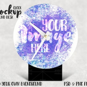 May include: A white round clock with a purple and blue watercolor design. The clock face has the words "Your Image Here" written on it. The clock is sitting on a black stand.
