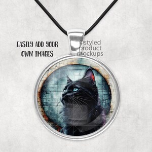 May include: A silver pendant necklace featuring a black cat image within a round glass cabochon. The cat has blue eyes and is gazing to the left. The background is an abstract design in shades of blue and grey.