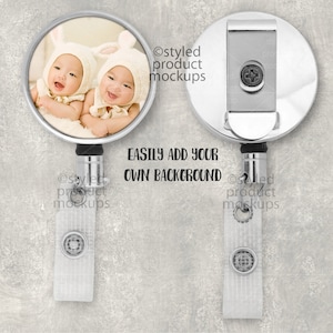 May include: A silver retractable badge holder with a round photo insert featuring two babies wearing white bunny hats. The text "EASILY ADD YOUR OWN BACKGROUND" is printed below the photo insert.