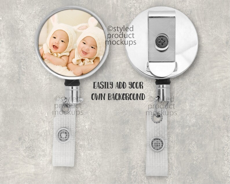 May include: A silver retractable badge holder with a round photo insert featuring two babies wearing white bunny hats. The text "EASILY ADD YOUR OWN BACKGROUND" is printed below the photo insert.