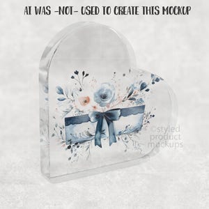 Pu&ograve; includere: Un blocco acrilico trasparente a forma di cuore con un design ad acquerello. Il design include una scatola blu con un fiocco, fiori e foglie. Il testo "AI WAS -NOT- USED TO CREATE THIS MOCKUP" &egrave; in alto.