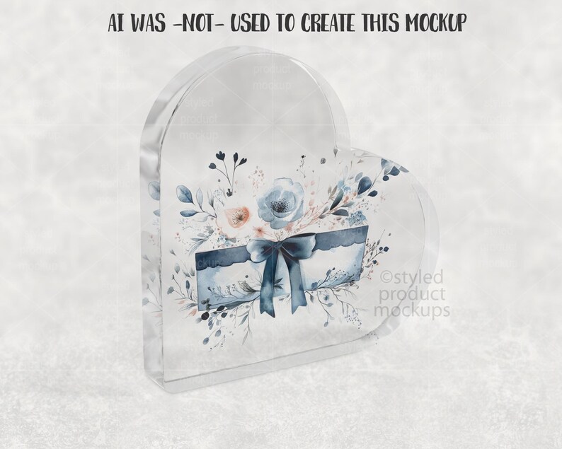 Pu&ograve; includere: Un blocco acrilico trasparente a forma di cuore con un design ad acquerello. Il design include una scatola blu con un fiocco, fiori e foglie. Il testo "AI WAS -NOT- USED TO CREATE THIS MOCKUP" &egrave; in alto.