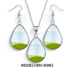 May include: A silver-toned necklace and earring set. The teardrop-shaped pendants and earrings feature a landscape design with a green field, blue sky, and white clouds. The text "INCLUDES CANVA FRAMES" is at the bottom.