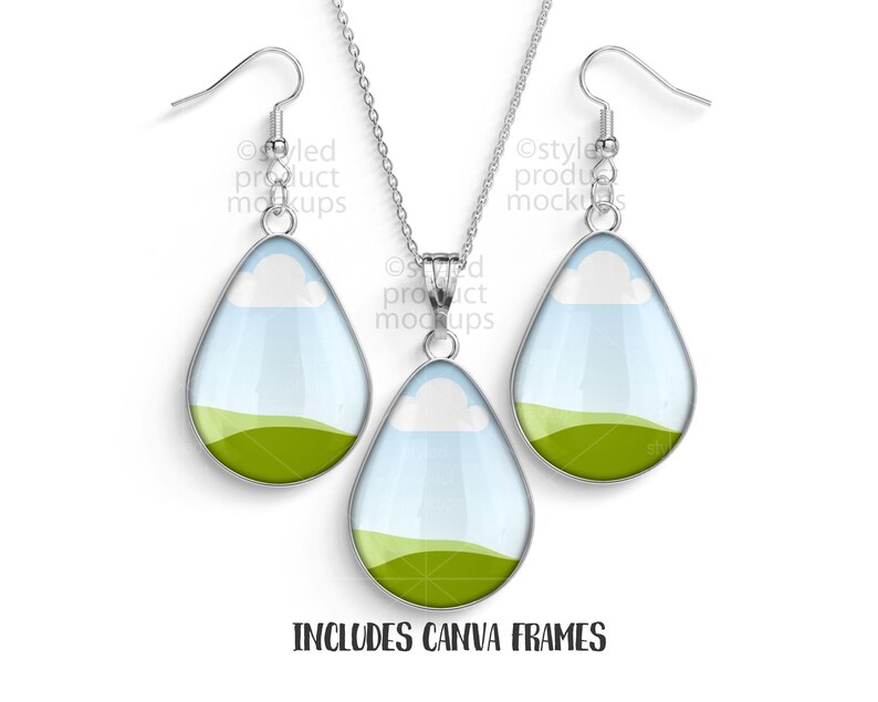 May include: A silver-toned necklace and earring set. The teardrop-shaped pendants and earrings feature a landscape design with a green field, blue sky, and white clouds. The text "INCLUDES CANVA FRAMES" is at the bottom.