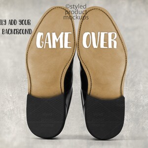 May include: A pair of black leather dress shoes with the words "GAME OVER" printed in white on the soles. The image includes the text "EASILY ADD YOUR OWN BACKGROUND" and "styled product mockups".
