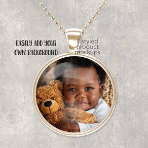 May include: A gold chain necklace with a round pendant featuring a photo of a young child holding a teddy bear. The pendant has a clear glass front and a gold metal frame.
