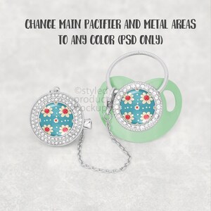 May include: A mint green baby pacifier with a floral design on the front, a silver chain, and a matching clip. The floral design features red and yellow flowers on a teal background, surrounded by a ring of clear rhinestones.
