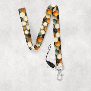 May include: A lanyard with a geometric honeycomb pattern in shades of orange, brown, and cream. The lanyard has a black plastic clasp and a silver-colored metal clip for attaching keys or an ID badge.