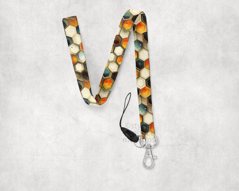 May include: A lanyard with a geometric honeycomb pattern in shades of orange, brown, and cream. The lanyard has a black plastic clasp and a silver-colored metal clip for attaching keys or an ID badge.