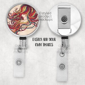 May include: A silver retractable badge holder with a white strap. The front of the holder features a round, colorful design of a woman's face with flowing hair. The text "EASILY ADD YOUR OWN IMAGES" is printed below the holder.