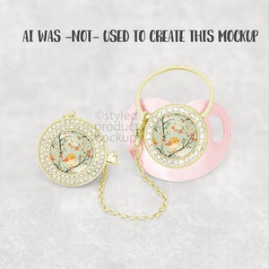 May include: A pink baby pacifier and matching pacifier clip. Both feature a gold-colored bezel encrusted with rhinestones. The center of each has a floral design with a small orange bird. The pacifier clip has a gold chain.