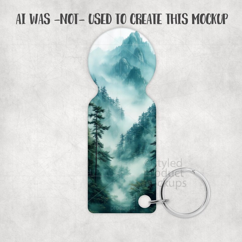 May include: Keyring with a mountain landscape design in shades of teal and white. The keyring has a silver-colored metal ring and a white attachment. The text "AI WAS -NOT- USED TO CREATE THIS MOCKUP" is at the top.
