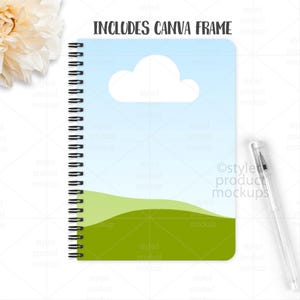 May include: A spiral-bound notebook with a sky and landscape design. The cover features a blue sky with a white cloud and green hills. The text "INCLUDES CANVA FRAME" is at the top. A clear pen rests on the right side.