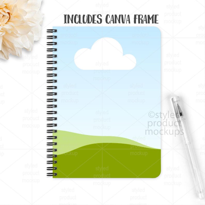 May include: A spiral-bound notebook with a sky and landscape design. The cover features a blue sky with a white cloud and green hills. The text "INCLUDES CANVA FRAME" is at the top. A clear pen rests on the right side.