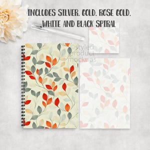 Op de afbeelding: Een spiraalgebonden notitieboek, een notitieblok en een kleine kaart met een bladpatroon in rood, oranje en grijs op een cr&egrave;mekleurige achtergrond. De tekst "INCLUDES SILVER, GOLD, ROSE GOLD, WHITE AND BLACK SPIRAL" staat bovenaan. Een pen is ook inbegrepen.