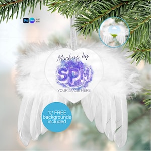 May include: A heart-shaped ornament with white feather wings and a silver ribbon for hanging. The ornament has the text "Mockup by SPM YOUR IMAGE HERE" and a blue circle with the text "12 FREE backgrounds included".