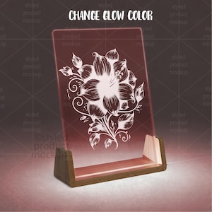 K&ouml;nnte beinhalten: Ein leuchtendes, rechteckiges Acrylschild mit floralem Design, das in einem Holzsockel steht. Das Schild zeigt eine wei&szlig;e Blumenillustration auf rotem Hintergrund. Der Text "CHANGE GLOW COLOR" steht oben.