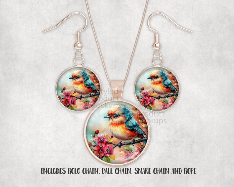 May include: A jewellery set comprising a pendant necklace and matching earrings. Each piece features a round, silver-toned frame with a colourful bird illustration perched on a flowering branch. The bird has blue, orange, and yellow feathers. The text in the image says "INCLUDES ROLO CHAIN, BALL CHAIN, SNAKE CHAIN AND ROPE."