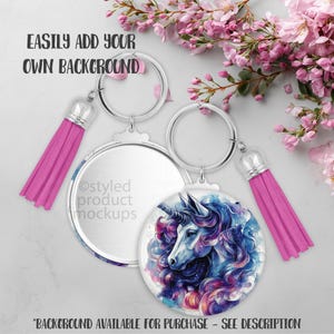 May include: Two round keychains with silver-tone metal rims and pink tassels. One keychain features a watercolor unicorn design in blue, purple, and pink. The text "EASILY ADD YOUR OWN BACKGROUND" is visible. "BACKGROUND AVAILABLE FOR PURCHASE - SEE DESCRIPTION" is also visible.