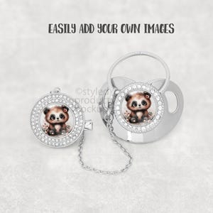 May include: A silver baby pacifier and clip set. Each piece features a round design with a cute panda bear illustration surrounded by clear rhinestones. A small chain connects the clip to the pacifier.