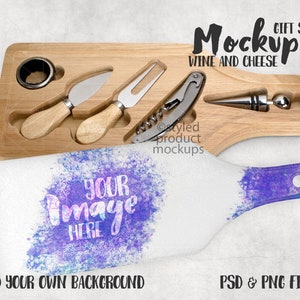 May include: A wooden cheese board with a wine bottle stopper, a corkscrew, two cheese knives, and a ring opener. The board is on a white surface with a purple and blue watercolor design. The text "Mockup Gift Set Wine and Cheese" is at the top of the image.
