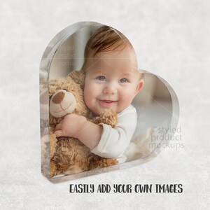 Pu&ograve; includere: Una cornice a forma di cuore trasparente con un bambino sorridente che tiene un orsacchiotto. Il bambino indossa una tutina bianca. Il testo "EASILY ADD YOUR OWN IMAGES" &egrave; in basso.