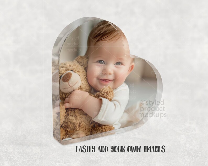 Pu&ograve; includere: Una cornice a forma di cuore trasparente con un bambino sorridente che tiene un orsacchiotto. Il bambino indossa una tutina bianca. Il testo "EASILY ADD YOUR OWN IMAGES" &egrave; in basso.