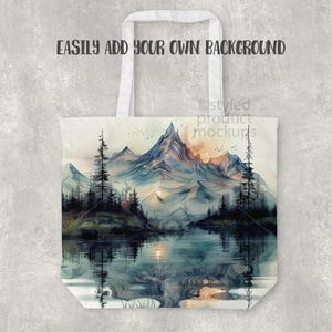 Pu&ograve; includere: Una borsa tote bianca con un design paesaggistico ad acquerello con montagne, un lago e alberi. La borsa ha manici bianchi e il testo "EASILY ADD YOUR OWN BACKGROUND".