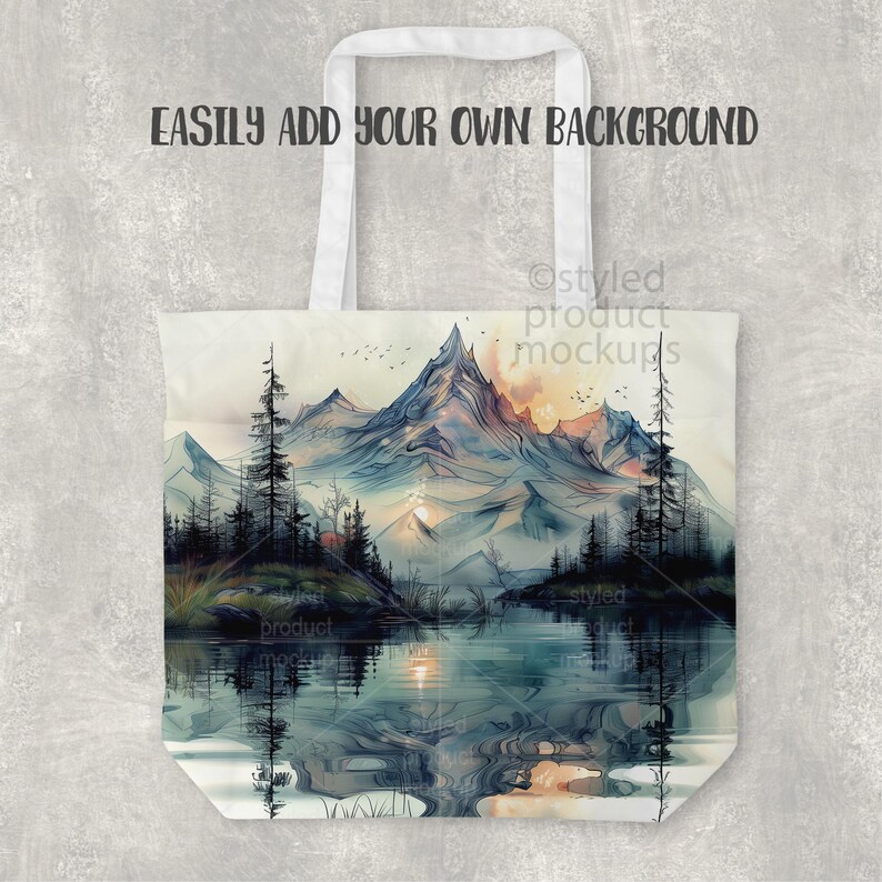 Pu&ograve; includere: Una borsa tote bianca con un design paesaggistico ad acquerello con montagne, un lago e alberi. La borsa ha manici bianchi e il testo "EASILY ADD YOUR OWN BACKGROUND".